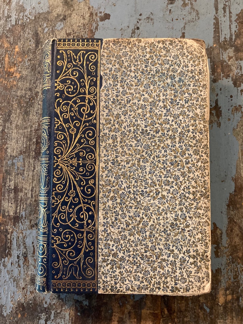 May include: A vintage book with a dark blue cover and gold-colored floral designs. The book has a patterned paper cover with a floral design.