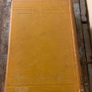 May include: A vintage book with a yellow cover and intricate embossed designs. The cover features a floral pattern and a decorative border.