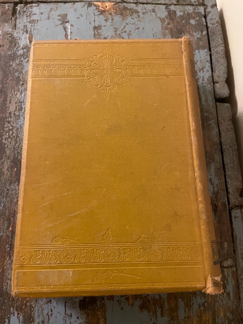 May include: A vintage book with a yellow cover and intricate embossed designs. The cover features a floral pattern and a decorative border.