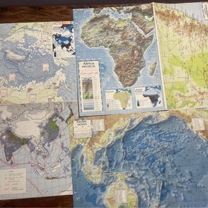 May include: Four vintage maps of the world, including Eurasia Vegetation, Africa Physical, and the Pacific Ocean. The maps are printed on paper and have a faded, antique look.