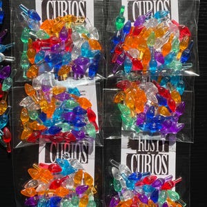 May include: Five bags of colorful plastic Christmas light bulb tips. Each bag contains a variety of colors, including red, green, blue, yellow, orange, and purple. The bags are labeled "Rusty Curios".