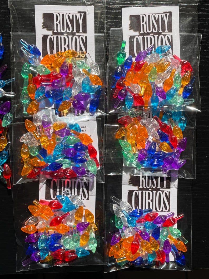 May include: Five bags of colorful plastic Christmas light bulb tips. Each bag contains a variety of colors, including red, green, blue, yellow, orange, and purple. The bags are labeled "Rusty Curios".