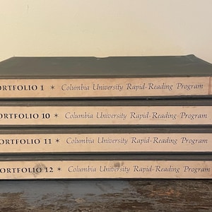 May include: Four gray portfolios stacked on top of each other. Each portfolio has a label that reads "PORTFOLIO" followed by a number and "Columbia University Rapid-Reading Program". The portfolios are vintage and show signs of wear.