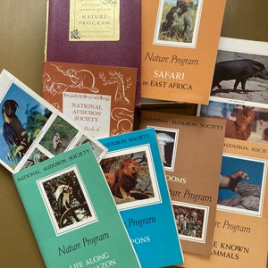 May include: A collection of vintage National Audubon Society nature program books with colorful covers featuring images of animals and text about the program. The books include titles like "Safari in East Africa", "Life Along the Amazon", and "Mushrooms".