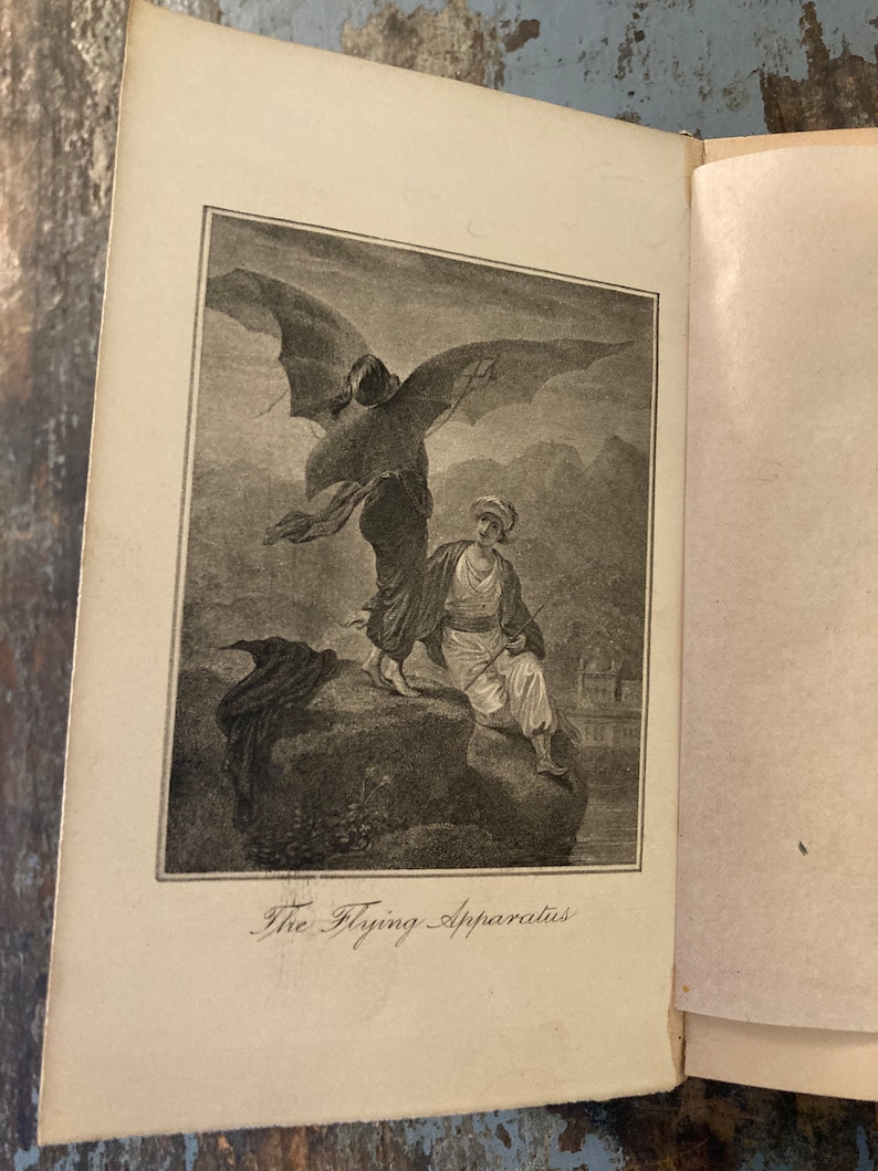 May include: A black and white illustration of a person flying with a large, bat-like apparatus. The person is wearing a long, flowing robe and has a long, flowing beard. The apparatus has large, bat-like wings and a long, thin tail. The illustration is titled "The Flying Apparatus".