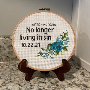Puede incluir: Un aro de bordado blanco con un dise&ntilde;o floral azul y verde. El aro tiene el texto "Nate + Meagan No longer living in sin 10.22.21" bordado en &eacute;l.