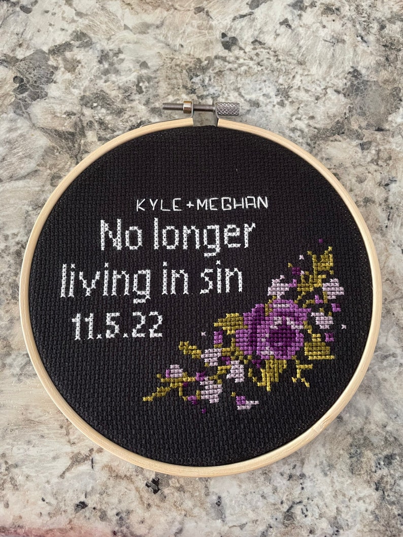 Puede incluir: Aro de bordado negro con el texto "KYLE + MEGHAN No longer living in sin 11.5.22" y un dise&ntilde;o floral morado y dorado.