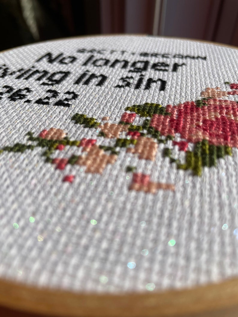 Puede incluir: Aro de bordado blanco con el texto "No longer living in sin 12.22" en hilo negro. El aro est&aacute; decorado con un dise&ntilde;o floral en hilo rosa, verde y marr&oacute;n.