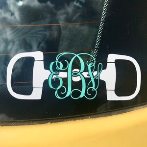 May include: A white equestrian stirrup decal with a teal monogram of the letters "B & Y" on a black car window.