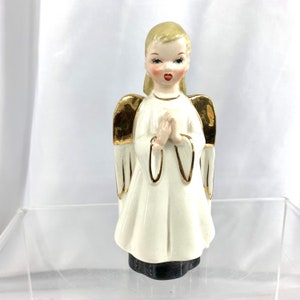 May include: A white porcelain angel figurine with gold wings and a white dress. The angel has blonde hair and is praying with her hands clasped together.