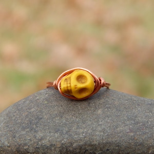 May include: A yellow skull bead wrapped in copper wire to create a ring.