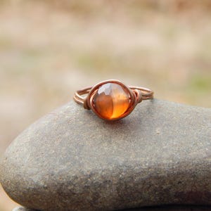 May include: A copper wire wrapped ring with an orange gemstone.