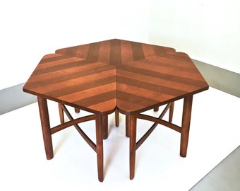 May include: A set of four wooden nesting tables with a chevron pattern on the top. The tables are arranged in a star shape and are made of a dark brown wood.