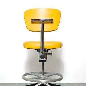May include: A yellow office chair with a chrome base and adjustable height. The chair has a padded seat and backrest and features a footrest.