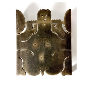May include: A gold-colored metal wall sculpture with a stylized human figure design. The sculpture has a cutout design and is abstract in style.