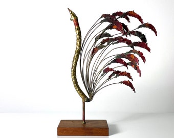 May include: A gold metal sculpture of a bird with red and orange feathers. The sculpture is on a wooden base.