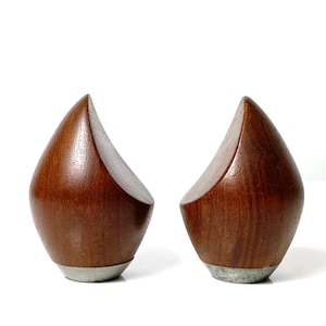 May include: A pair of wooden bookends shaped like teardrops with a silver base. The bookends are a dark brown color.
