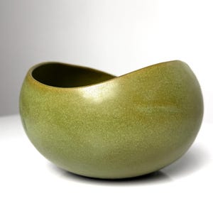 May include: A green ceramic bowl with a rounded, organic shape. The bowl has a textured, speckled surface.