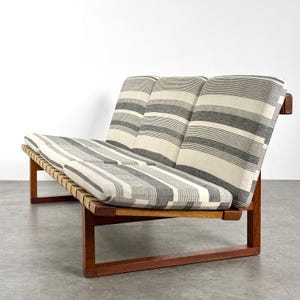 May include: A mid-century modern two-seater sofa with a wooden frame and striped cushions. The cushions feature a pattern of alternating gray and white horizontal stripes. The wooden frame has a warm, reddish-brown finish.