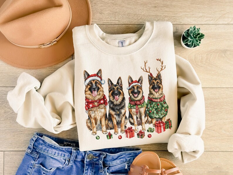 May include: A cream-colored sweatshirt with a Christmas-themed design featuring four German Shepherd dogs wearing Santa hats and reindeer antlers. The dogs are surrounded by red and green Christmas decorations.