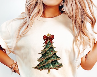 以下が含まれることがあります： 緑のクリスマスツリーのデザインが施された白いTシャツ。ツリーは金色のキラキラと赤いオーナメント、赤いリボンで飾られています。