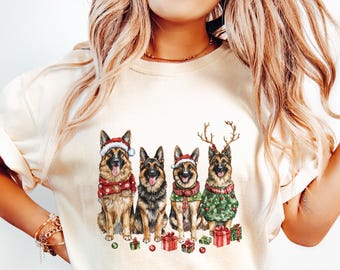 May include: A white t-shirt featuring a Christmas design with four German Shepherd dogs wearing Santa hats and reindeer antlers. The dogs are surrounded by presents and green and red baubles.