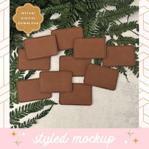 May include: A mockup of eight brown leather labels with stitched edges, arranged on a white surface with green foliage.