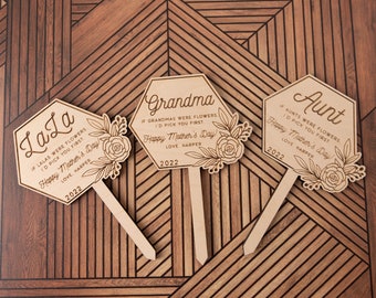 May include: Three wooden hexagonal garden stakes with floral designs and personalized messages for Mother's Day. The stakes read "LaLa", "Grandma", and "Aunt" with a personalized message and the year 2022.