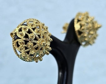 May include: A pair of gold earrings with a delicate, intricate design. The earrings are displayed on a black stand against a blue background.