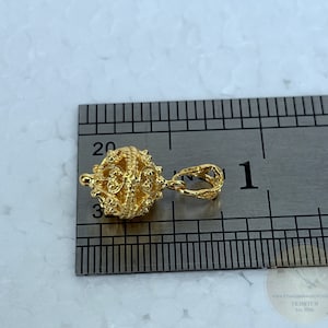 May include: Gold-toned pendant charm with a detailed, intricate design. The charm is approximately 1 inch in diameter and features a loop for attaching to a necklace or bracelet.