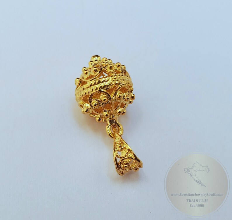 May include: A gold pendant with a round, intricate design. The pendant is made of filigree and has a delicate, ornate look.