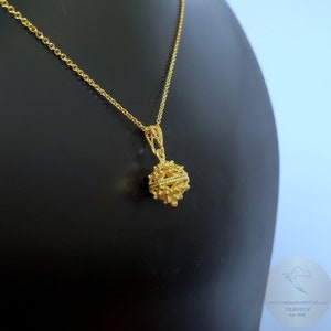 May include: A gold chain necklace with a delicate, intricate gold pendant in the shape of a sphere. The pendant has a textured surface and appears to be made of multiple interwoven strands.
