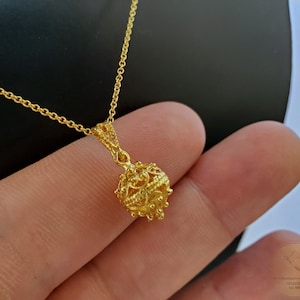 May include: A gold chain necklace with a delicate, intricate, round pendant. The pendant is made of gold and has a filigree design.