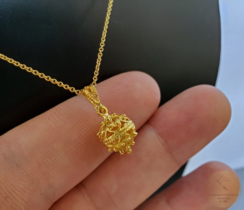 May include: A gold chain necklace with a delicate, intricate, round pendant. The pendant is made of gold and has a filigree design.