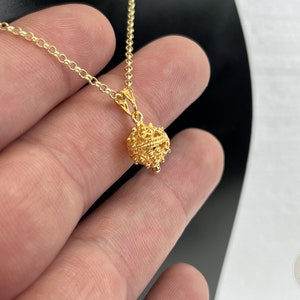 May include: A gold chain necklace with a delicate, ornate, round pendant. The pendant is made of intricate, filigree-like designs.