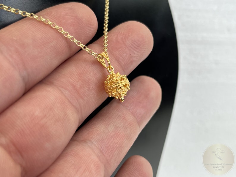 May include: A gold chain necklace with a delicate, ornate, round pendant. The pendant is made of intricate, filigree-like designs.