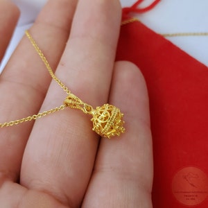 May include: A gold chain necklace with a delicate, ornate pendant. The pendant is a small, round ball with intricate designs and a textured surface.