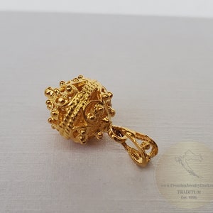 May include: A gold pendant with a detailed, intricate design. The pendant is round and has a small loop at the top for attaching to a chain.