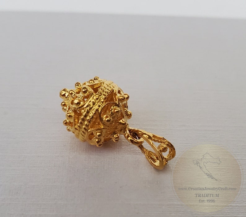 May include: A gold pendant with a detailed, intricate design. The pendant is round and has a small loop at the top for attaching to a chain.