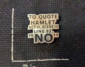 May include: A silver-colored pin with the quote "TO QUOTE HAMLET ACT III, SCENE III LINE 92, 'NO'" in black text. The pin is approximately 2 inches wide and is set against a dark, textured background.
