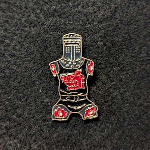 Peut inclure: Épinglette en émail noir représentant un chevalier en armure avec un dragon rouge sur la poitrine. Le chevalier porte un casque avec une visière et a une bordure dorée.