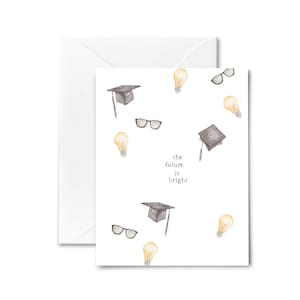 May include: A white card with a graduation cap, light bulbs, and eyeglasses printed on it. The text "the future is bright" is written in the center of the card.