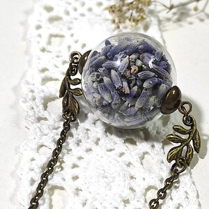May include: A delicate necklace featuring a glass orb filled with dried lavender flowers. The orb is attached to a bronze chain with leaf-shaped accents.