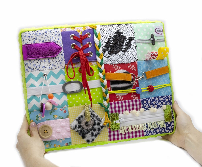 May include: A multi-colored fabric activity book with various textures and objects for babies and toddlers to explore. It features a zipper, buttons, laces, a buckle, and a variety of fabrics.