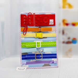 Puede incluir: Un tablero de tela colorido con varias texturas y cierres para que los ni&ntilde;os jueguen. Cuenta con un bot&oacute;n de fieltro rojo, una cremallera, una hebilla, un cord&oacute;n y varios tipos de cinturones.