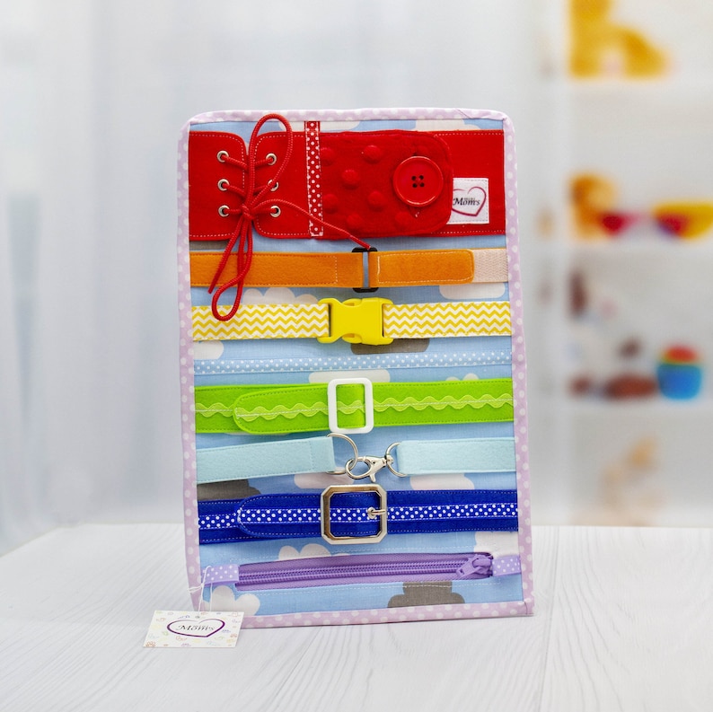 Puede incluir: Un tablero de tela colorido con varias texturas y cierres para que los ni&ntilde;os jueguen. Cuenta con un bot&oacute;n de fieltro rojo, una cremallera, una hebilla, un cord&oacute;n y varios tipos de cinturones.