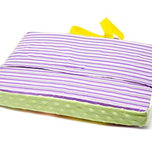 May include: A purple and white striped cushion with a green and yellow border. The cushion has a yellow handle.