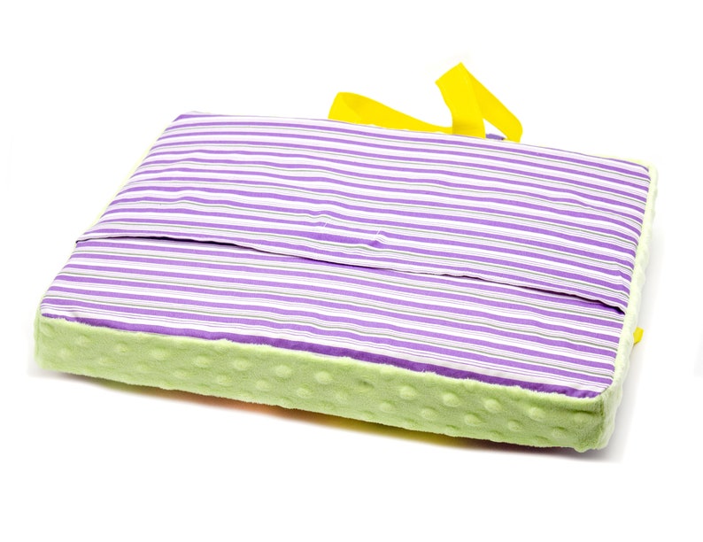 May include: A purple and white striped cushion with a green and yellow border. The cushion has a yellow handle.
