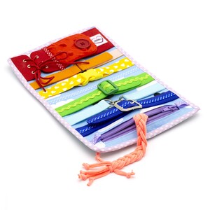 Puede incluir: Un libro de actividades de tela con colores de arco&iacute;ris con varias texturas y cierres para ni&ntilde;os. Cuenta con una cremallera, cordones, hebillas y un bot&oacute;n. El libro est&aacute; hecho de tela suave y es perfecto para desarrollar la motricidad fina.