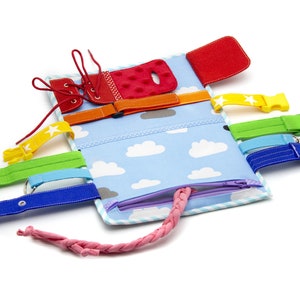 Puede incluir: Un libro de actividades de tela azul y blanco con una variedad de texturas y cierres para que los ni&ntilde;os exploren. Cuenta con una cremallera, cordones, hebillas y velcro.
